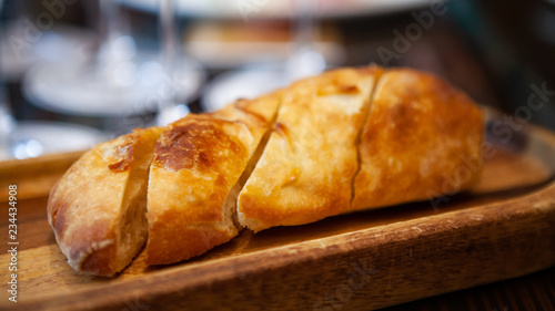 Freshly baked Italian Ciabatta bread from oven on a wooden tray for appetizer or meal starter. Looks tasty and delicious. Good source of carbohydrate. Not gluten-free. Natural light. Selective Focus.