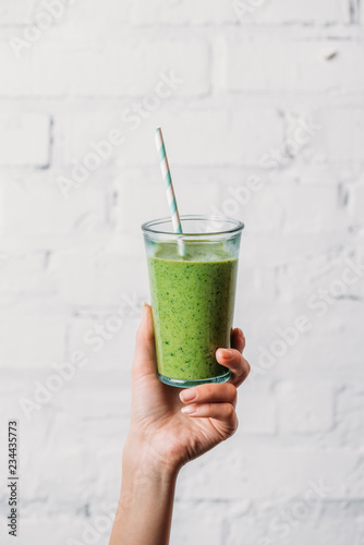 Female hand holding glass with green organic smoothie and straw