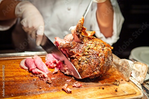 Professional chef carves a whole, roasted leg of lamb. An impressive centerpiece for party, Easter, Thanksgiving, Christmas and New Year celebration. Festive holiday and season greeting. Warm light.