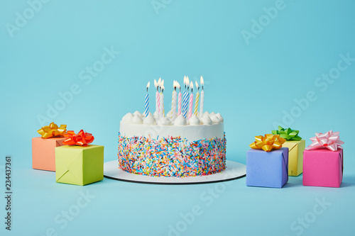 Delicious cake with candles  colorful gifts and confetti on blue background