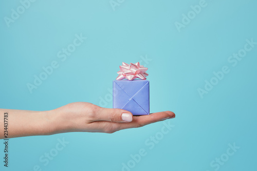 Fototapeta Naklejka Na Ścianę i Meble -  Partial view of woman holding gift with pink bow on blue background