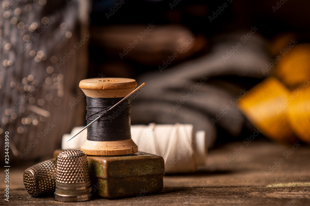 Close-up view of beautiful wooden sewing spool with thin black thread and  needle placed on rough wooden plank table with defocused tape measure on  background Stock Photo