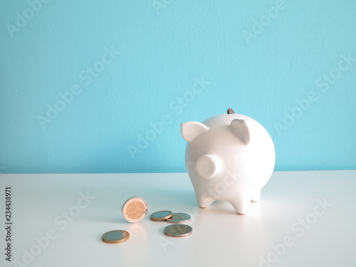 White ceramic piggy bank with euro coins on the table, with one coin in the back hole
