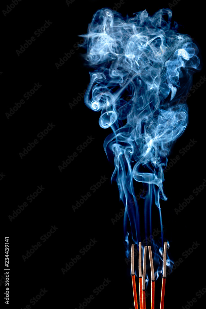 Closeup of calmly burning incense sticks with blue fume on black background Closeup of calmly burning incense sticks with blue fume on black background