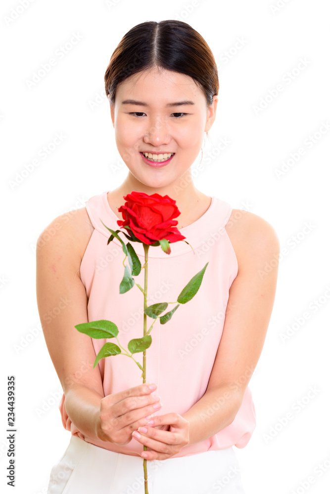 Studio shot of young happy Asian woman smiling and holding red r Studio shot of young happy Asian woman smiling and holding red r