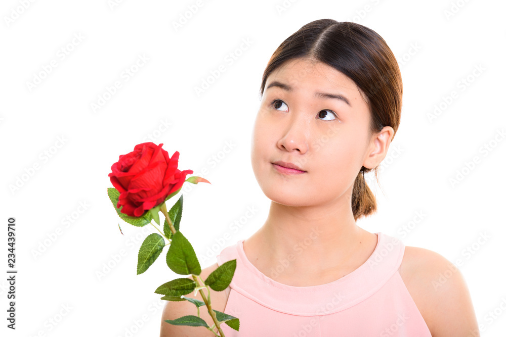 Studio shot of young beautiful Asian woman holding red rose whil