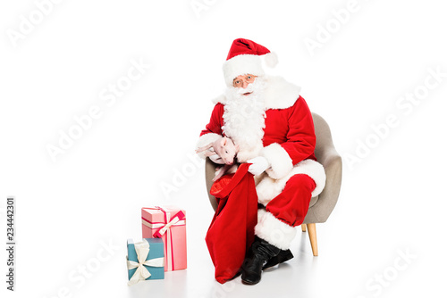 santa claus with presents sitting in armchair with little pig isolated on white © LIGHTFIELD STUDIOS