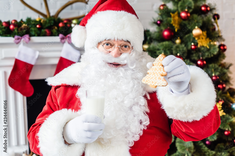 happy santa claus holding gingerbread cookie and glass of milk happy santa claus holding gingerbread cookie and glass of milk