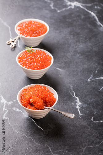 Red caviar Three species of salmon caviar in a white bowl on a black marble background. Variety of tastes.Seafood. Healthy Food Concept. Snack.Copy space for Text.
