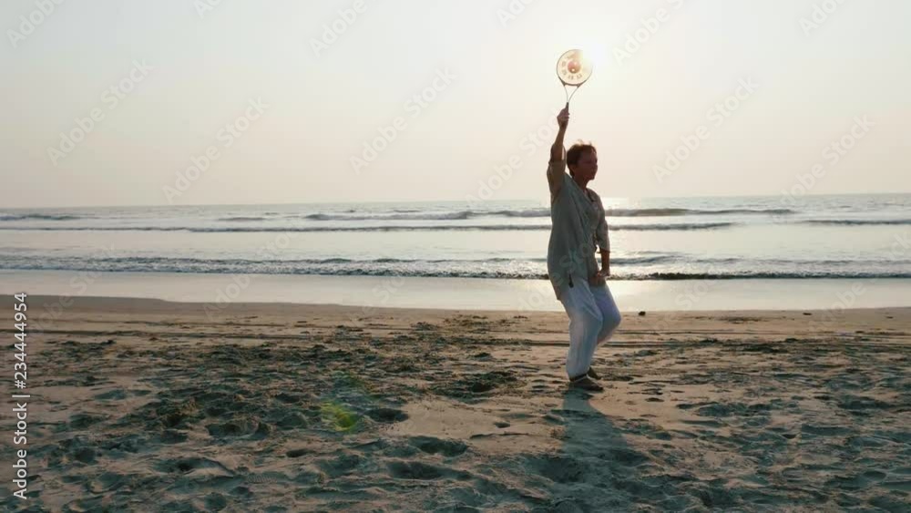 Senior woman practicing tai chi balloon ball on the beach at sunset