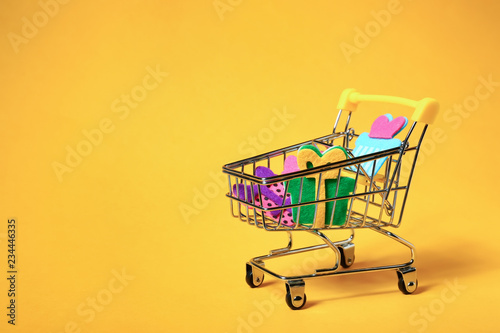 Shopping cart with decor on color background