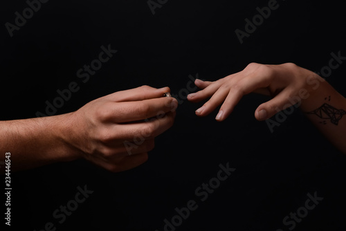Man putting engagement ring on fiancee's finger on dark background