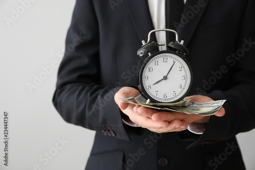 Businessman with clock and money on light background, closeup