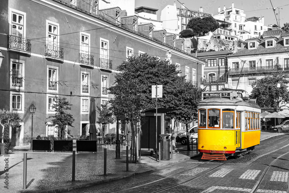 Fototapeta premium Yellow tram on old streets of Lisbon, Alfama, Portugal, popular touristic attraction and destination. Black and white picture with a coloured tram.