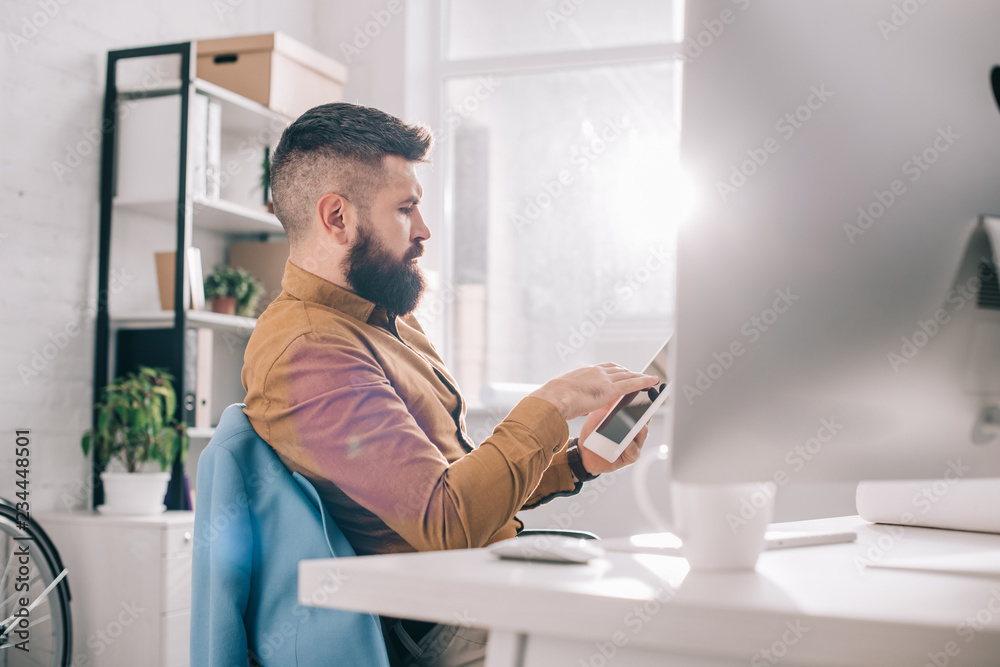 serious adult business man sitting at office desk and using digital tablet at workplace