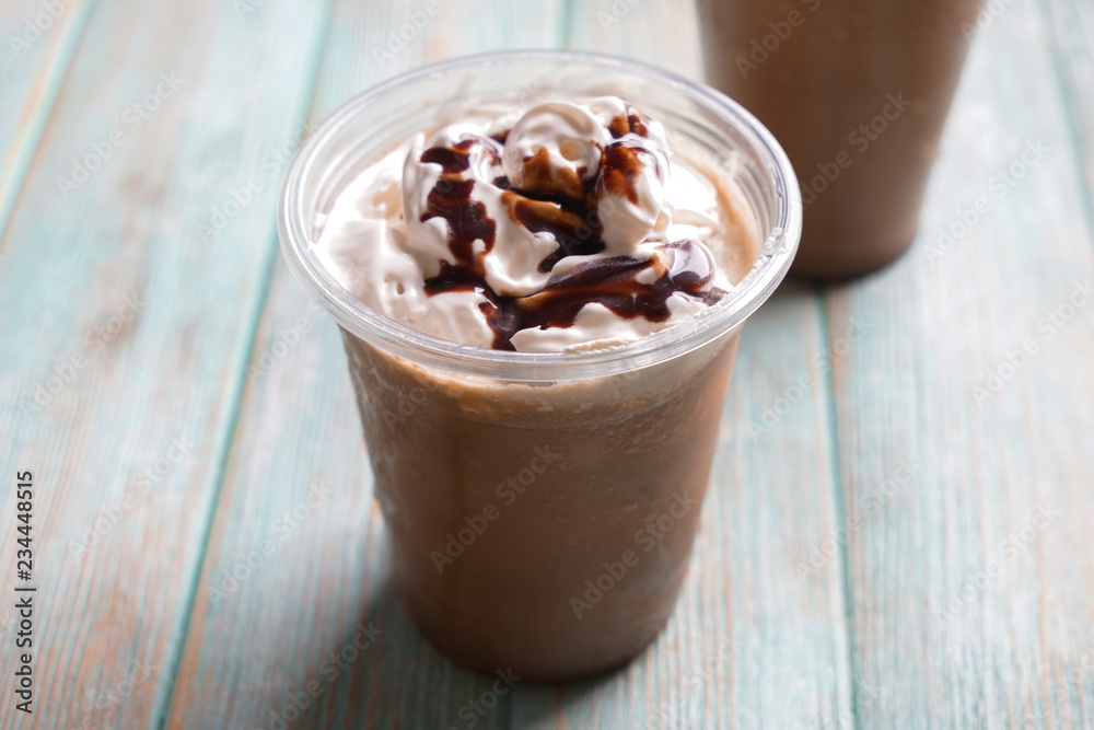 Cold coffee covered with whipped cream and chocolate in wet plastic cup on wooden table Cold coffee covered with whipped cream and chocolate in wet plastic cup on wooden table