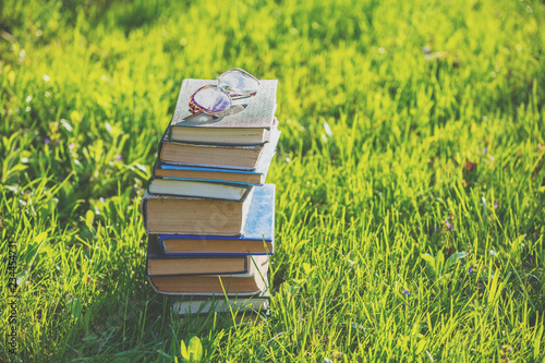 Очки лежат на пачка книг на открытом воздухе на зеленой траве весной