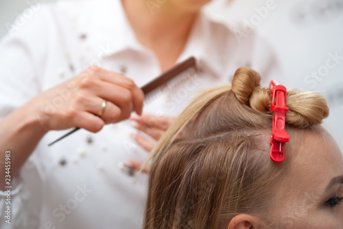 Professional hairdresser making a hairdo to a fair-haired model