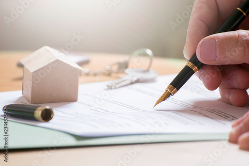 Man hand signing documentation for home mortgage with a pen. Keys and home icon with empty copy space for Editor's text.