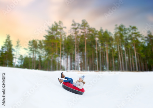 winter, leisure and entertainment concept - happy teenage girl sliding down hill on snow tube