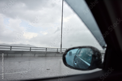Raindrop on a side mirror and a side window while a car is running on the slippery high way road with clear sky during a raining season.