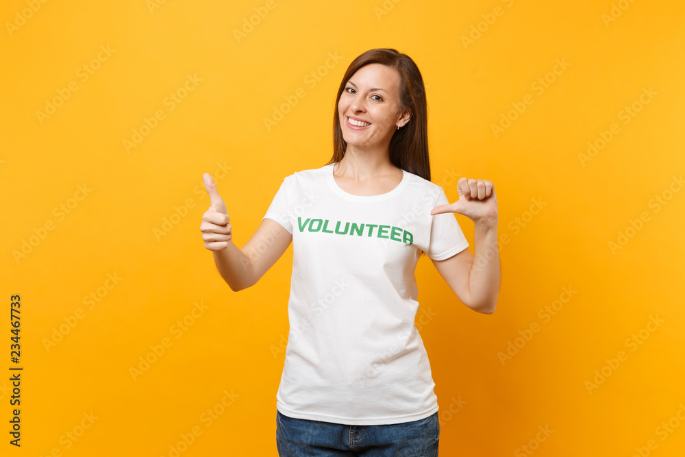 Portrait of happy smiling satisfied woman in white t-shirt with written inscription green title volunteer isolated on yellow background. Voluntary free assistance help, charity grace work concept. Portrait of happy smiling satisfied woman in white t-shirt with written inscription green title volunteer isolated on yellow background. Voluntary free assistance help, charity grace work concept.