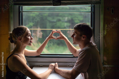 Couple of lovers traveling in train. Mood portrait of romantic pair in wagon looking at window with self reflections in it. Adventure on holiday of happy friends. Man and woman looking at each other. photo