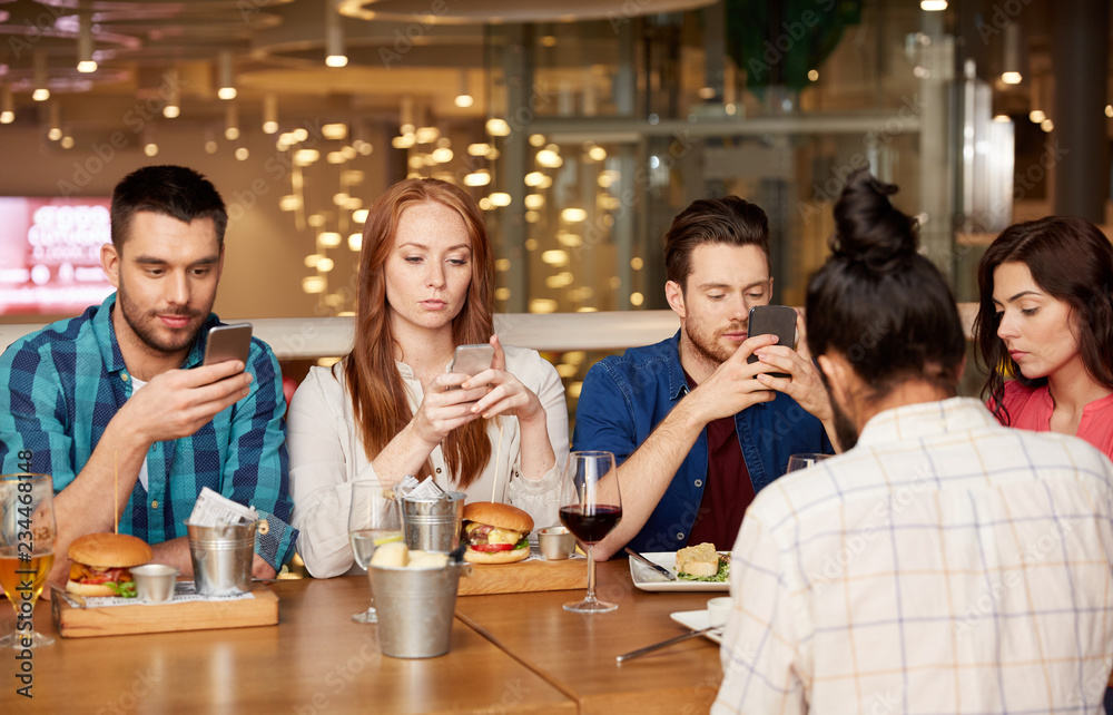 leisure, technology, lifestyle and people concept - friends with smartphones dining at restaurant