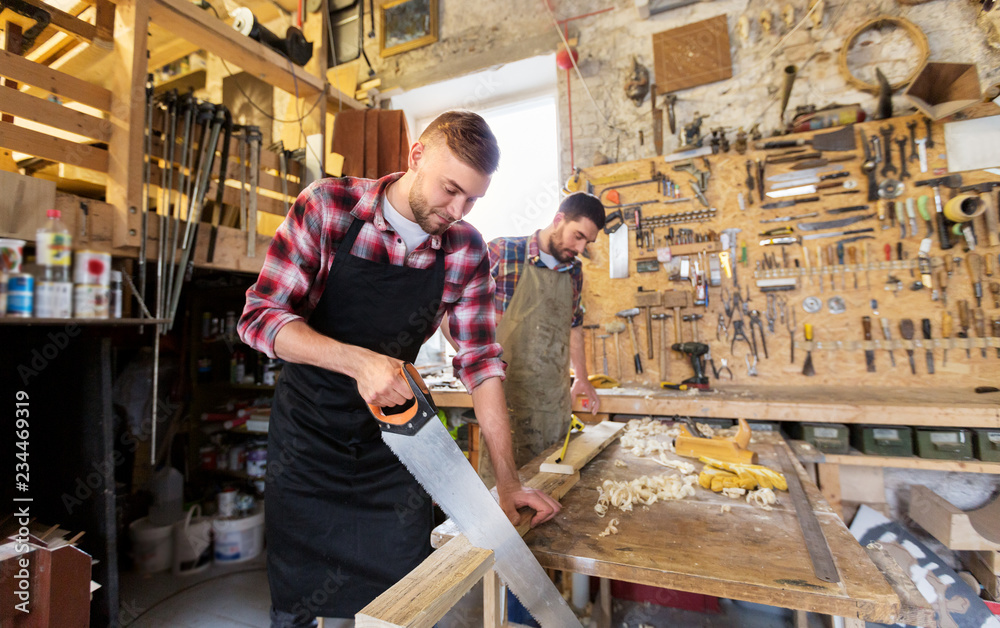 profession, carpentry, woodwork and people concept - two carpenters with saw and wood plank working at workshop profession, carpentry, woodwork and people concept - two carpenters with saw and wood plank working at workshop