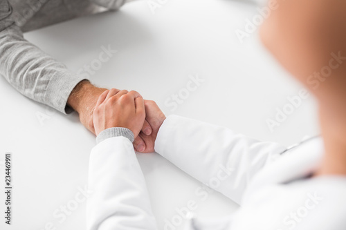 medicine, healthcare and old age concept - close up of young doctor holding senior patient hand
