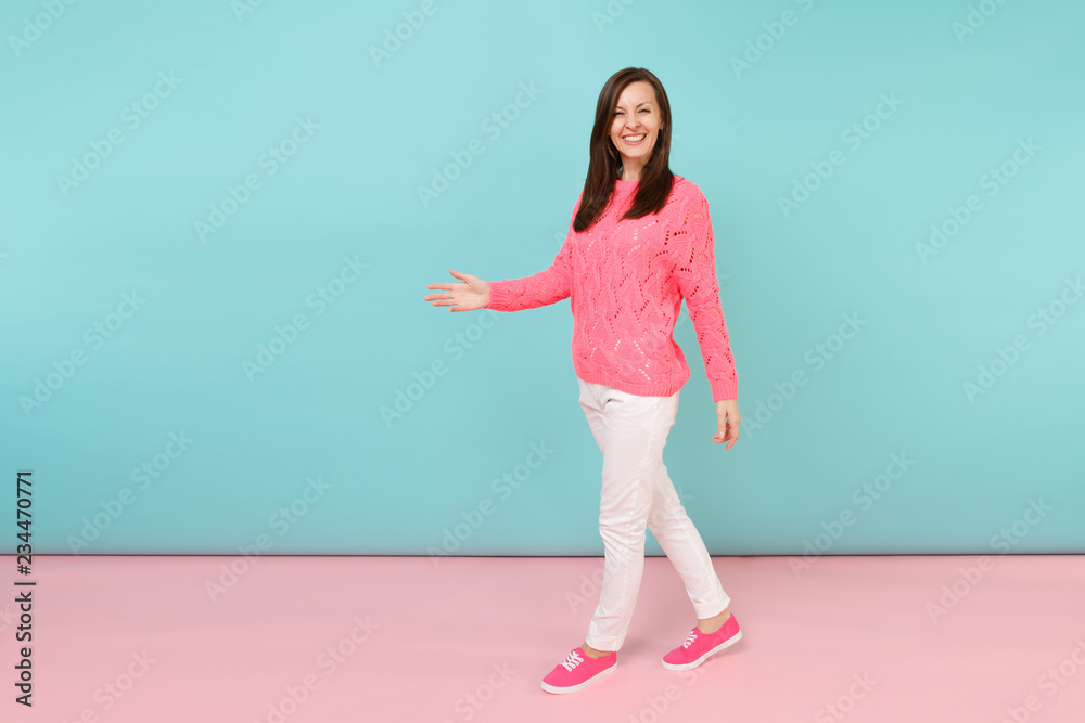 Full length portrait of smiling young woman in knitted rose sweater, white pants posing isolated on bright pink blue pastel wall background in studio. Fashion lifestyle concept. Mock up copy space. Full length portrait of smiling young woman in knitted rose sweater, white pants posing isolated on bright pink blue pastel wall background in studio. Fashion lifestyle concept. Mock up copy space.