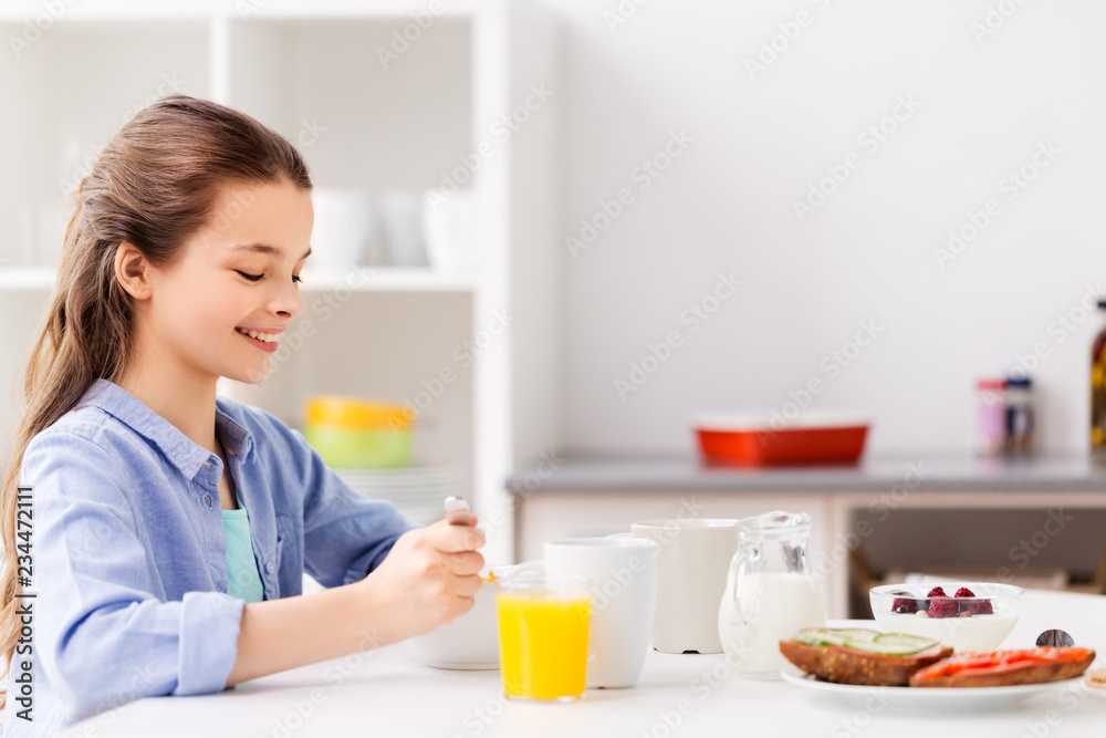 food, eating and people concept - happy girl having breakfast at home kitchen