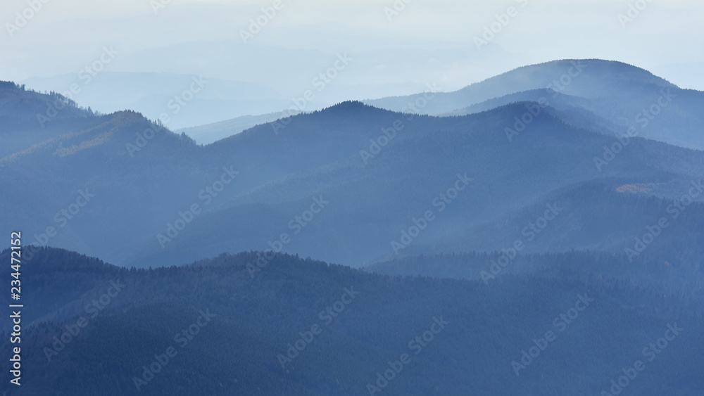 Peaceful blue nature background with foggy Bucegi mountains in Carpathians seen from Cota 2000, Sinaia resort, Romania