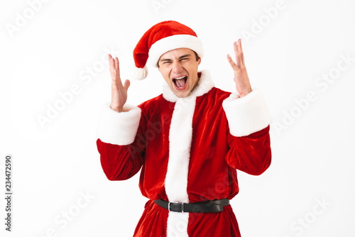 Portrait of ecstatic man 30s in santa claus costume and red hat screaming with gestures, isolated over white background in studio
