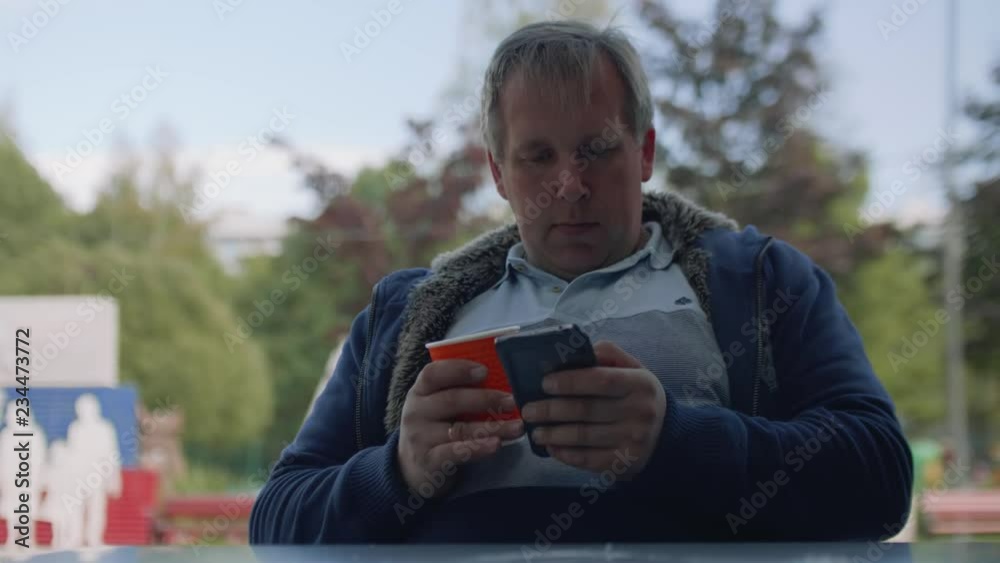 Man in t-shirt with paper cup of coffee surches internet in his smartphone Man in t-shirt with paper cup of coffee surches internet in his smartphone