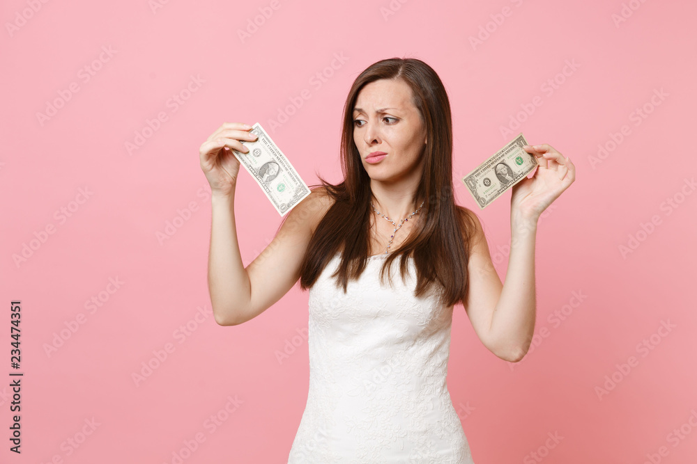 Portrait of disgusted upset bride woman in white wedding dress looking on one dollar bills isolated on pastel pink background. Lack of money. Organization of wedding celebration concept. Copy space. Portrait of disgusted upset bride woman in white wedding dress looking on one dollar bills isolated on pastel pink background. Lack of money. Organization of wedding celebration concept. Copy space.