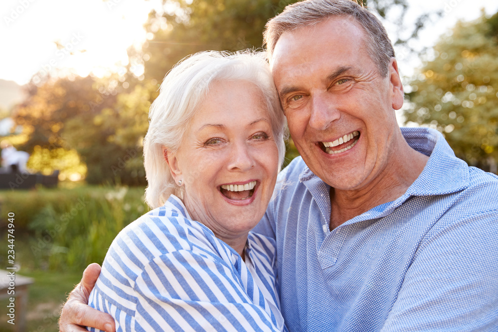 Portrait Of Loving Senior Couple Hugging Outdoors In Summer Park Against Flaring Sun Portrait Of Loving Senior Couple Hugging Outdoors In Summer Park Against Flaring Sun