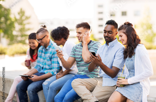 technology, friendship and international concept - group of friends with smartphones hanging out in summer city