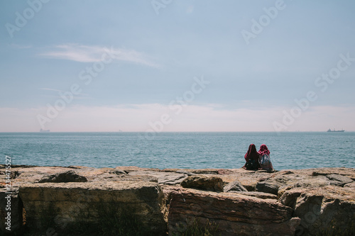 Two young Turkish girls in hijabs are sitting on the embankment of the Asian side of Istanbul, talking and admiring the sea. Istanbul, Turkey © Мария Шахматова