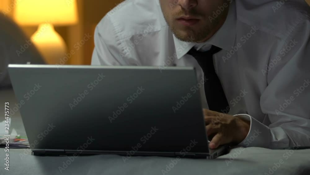 Man in business suit typing on laptop, lying on bed in hotel room, business trip Man in business suit typing on laptop, lying on bed in hotel room, business trip