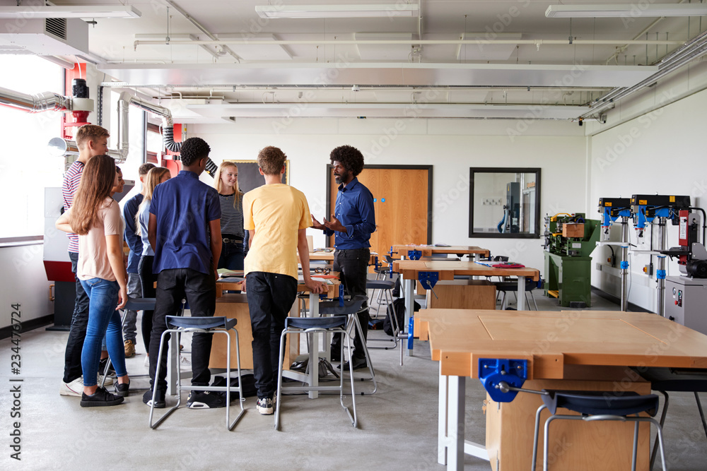 Group Of High School Students Standing Around Work Bench Listening To Teacher In Design And Technology Lesson - obrazy, fototapety, plakaty 