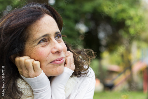 Portrait of middle aged woman with face resting on hands and visionary look. Closeup on pretty mature lady looking up thoughtful with positive expression