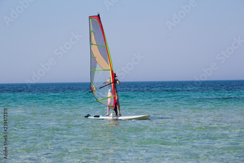 A woman windsurfing in the turquoise sea water in summer. © Nicole's