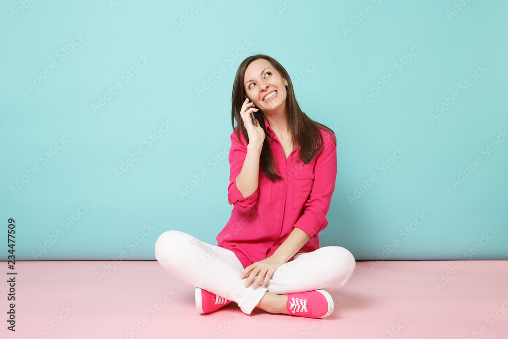 Full length portrait of young fun woman in rose shirt, white pants sit on floor hold cellphone isolated on bright pink blue pastel wall background studio. Fashion lifestyle concept. Mock up copy space Full length portrait of young fun woman in rose shirt, white pants sit on floor hold cellphone isolated on bright pink blue pastel wall background studio. Fashion lifestyle concept. Mock up copy space