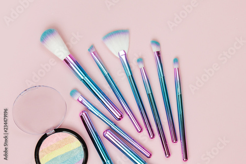 Fashion holographic colored makeup brushes with eye shadow and powder on a pastel pink background. Flat lay, top view