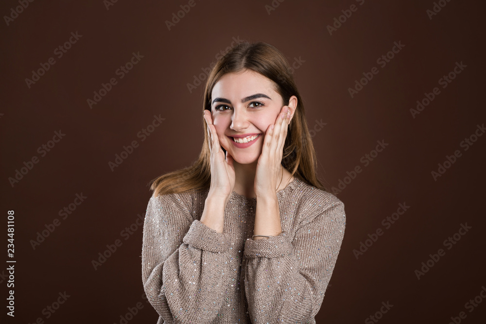 Pleasantly surprised woman looking with bugged eyes holding hands on cheeks opening her mouth in amazement not expecting to recieve such great present. Happy model isolated over brown background Pleasantly surprised woman looking with bugged eyes holding hands on cheeks opening her mouth in amazement not expecting to recieve such great present. Happy model isolated over brown background