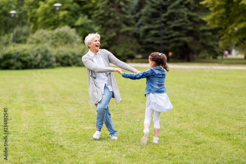 family, leisure and people concept - happy grandmother and granddaughter playing game or dancing at summer park photo