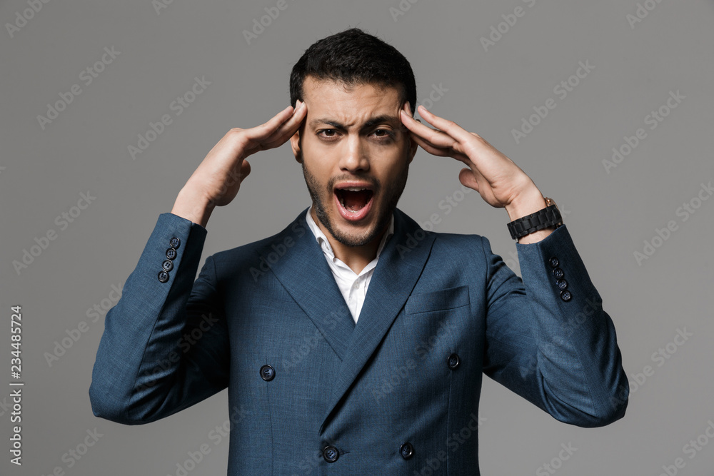 Aggressive screaming business man with headache posing isolated over grey wall background.