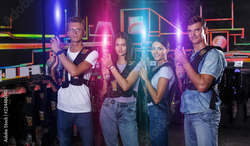 Portrait of positive young friends standing with laser guns duri