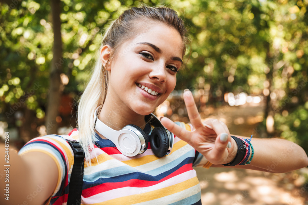 Obraz premium Happy cute young girl take a selfie by camera in park outdoors.